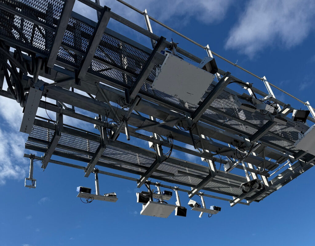 A steel overhead tolling system stretches over a road, outlined against a deep blue sky.