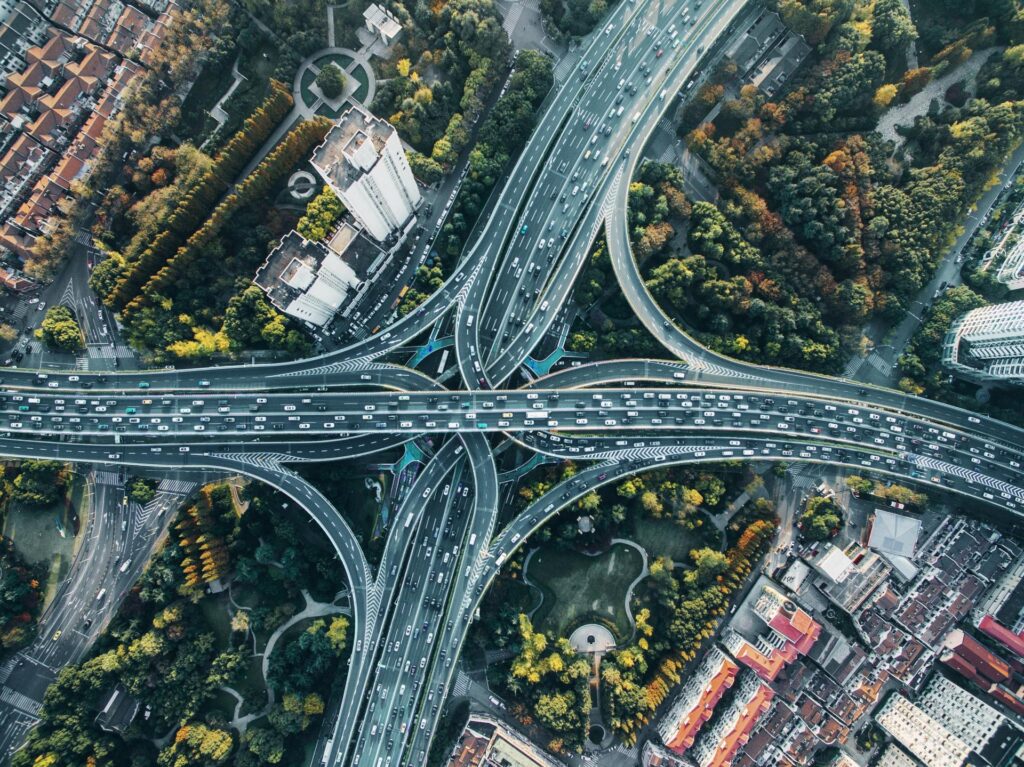 Overhead view of a complex highway system, winding over a series of parks where the trees are just starting to show autumnal color.