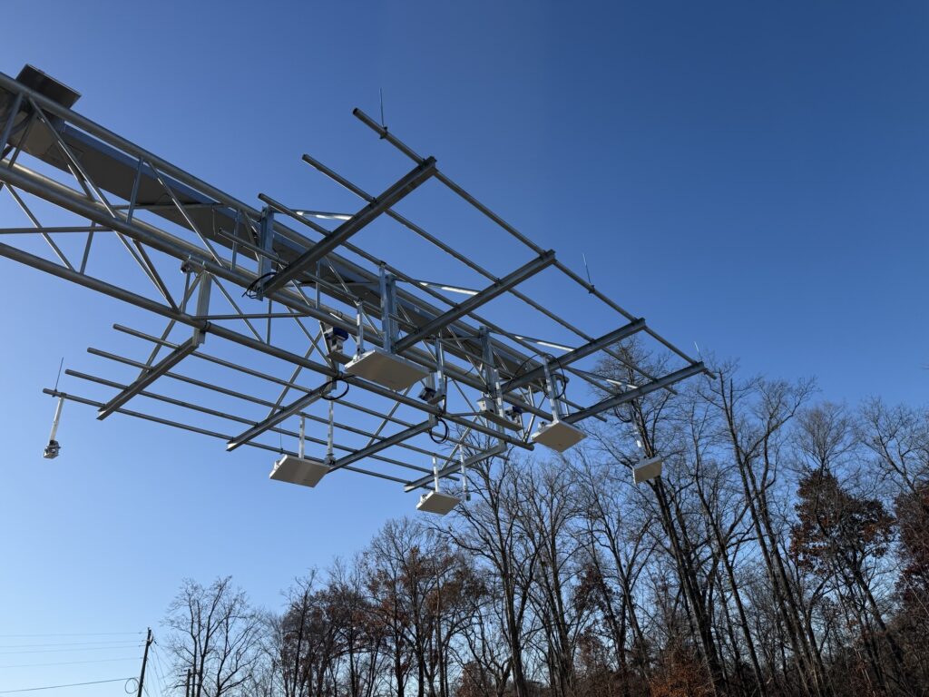 A view looking up at a V2X tolling structure against blue skies.