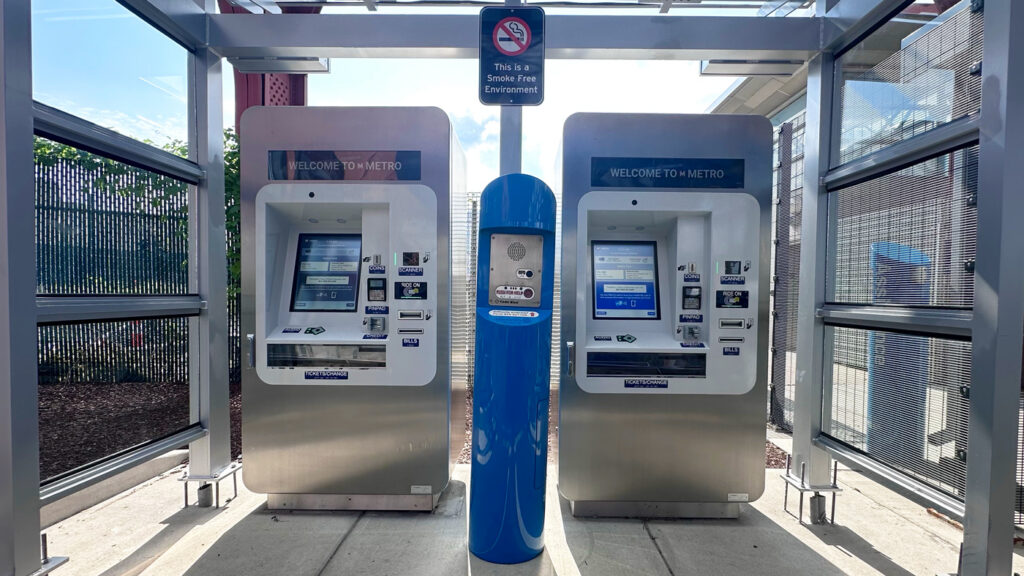 Two ticketing machines in modern stainless steel, blue, and white colors.